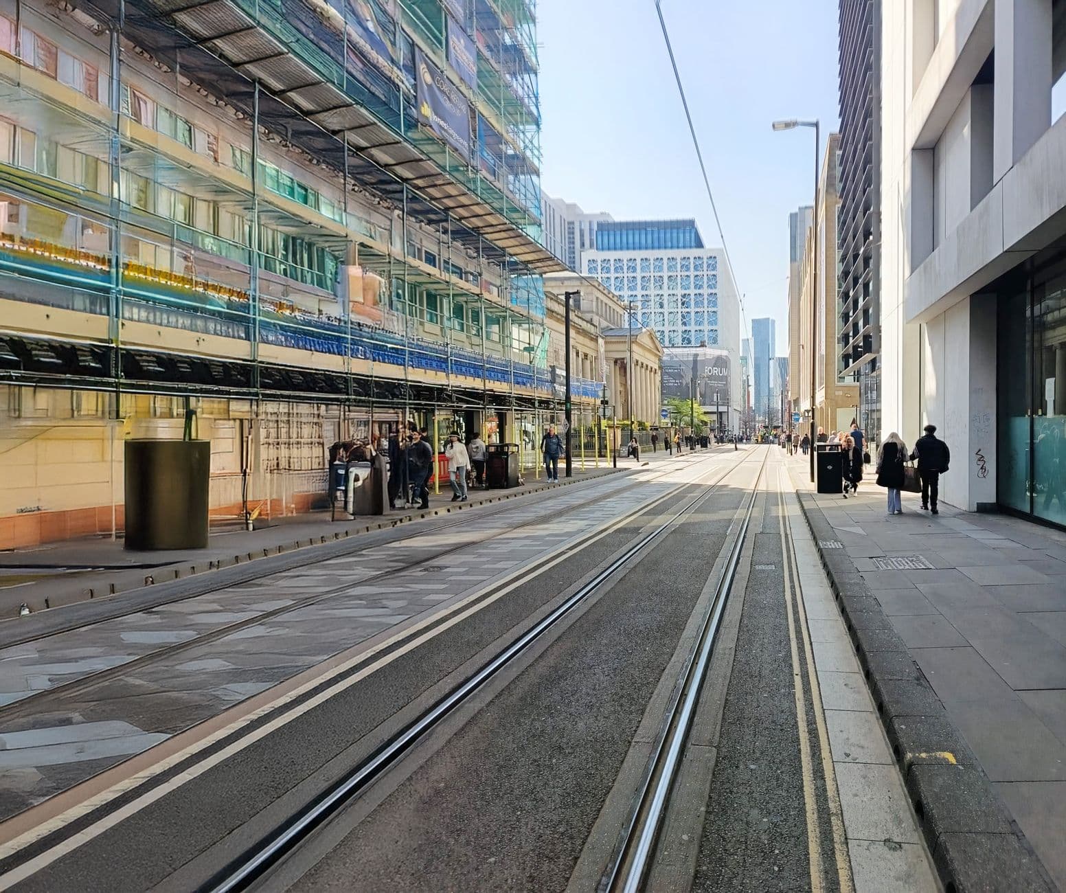 A bustling urban street with tram tracks and construction on a sunny day.